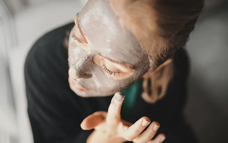 Ein junge Frau trägt sich im Gesicht eine Maske aus Heilerde auf.