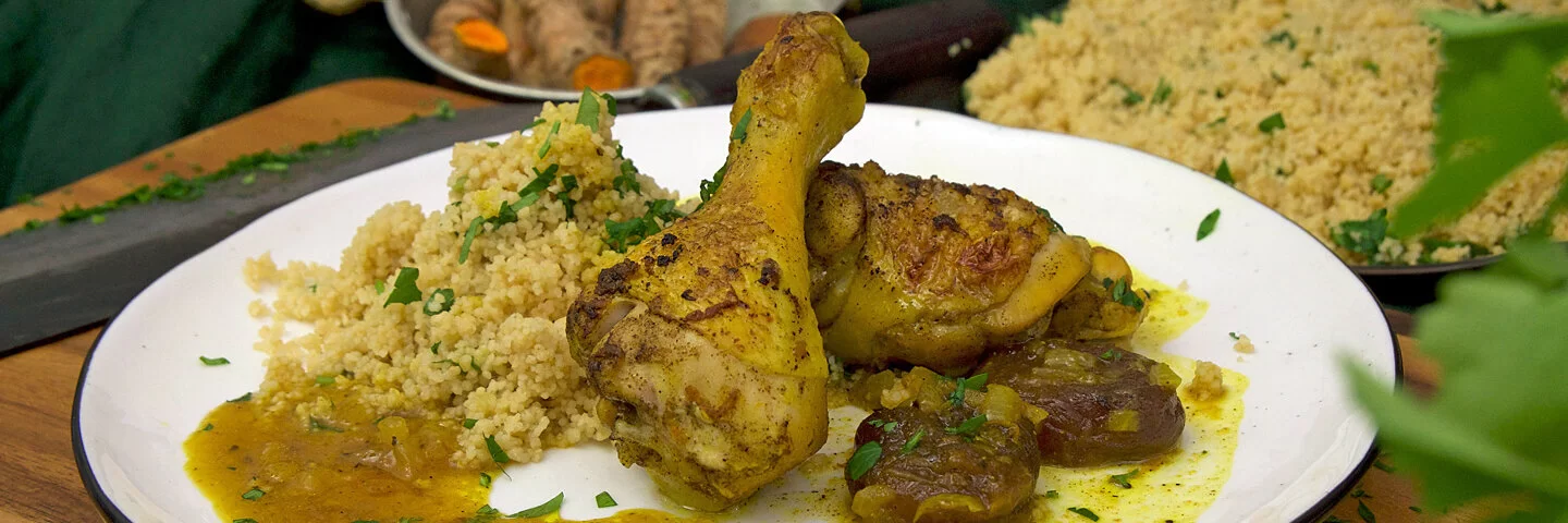 Kurkuma-Hähnchen in einer Soße aus Orangensaft und getrockneten Aprikosen mit Couscous und Petersilie auf einem weißen Teller, gekocht von Felicitas Then.