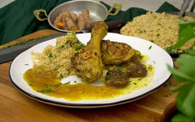 Kurkuma-Hähnchen in einer Soße aus Orangensaft und getrockneten Aprikosen mit Couscous und Petersilie auf einem weißen Teller, gekocht von Felicitas Then.