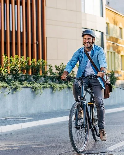 Ein Mann in Bürokleidung und mit Arbeitstasche fährt lächelnd mit dem Fahrrad durch die Stadt.