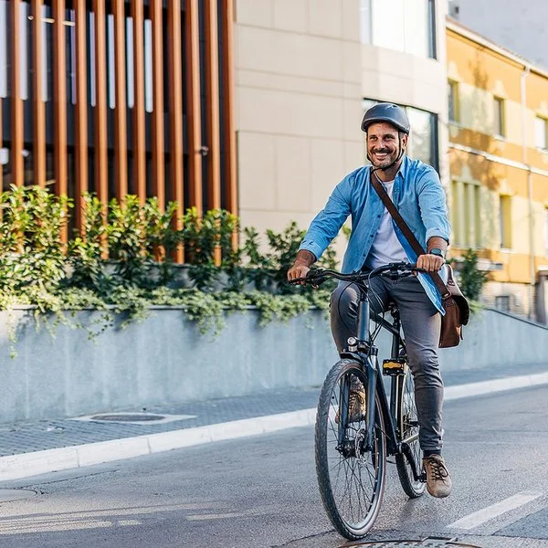 Ein Mann in Bürokleidung und mit Arbeitstasche fährt lächelnd mit dem Fahrrad durch die Stadt.