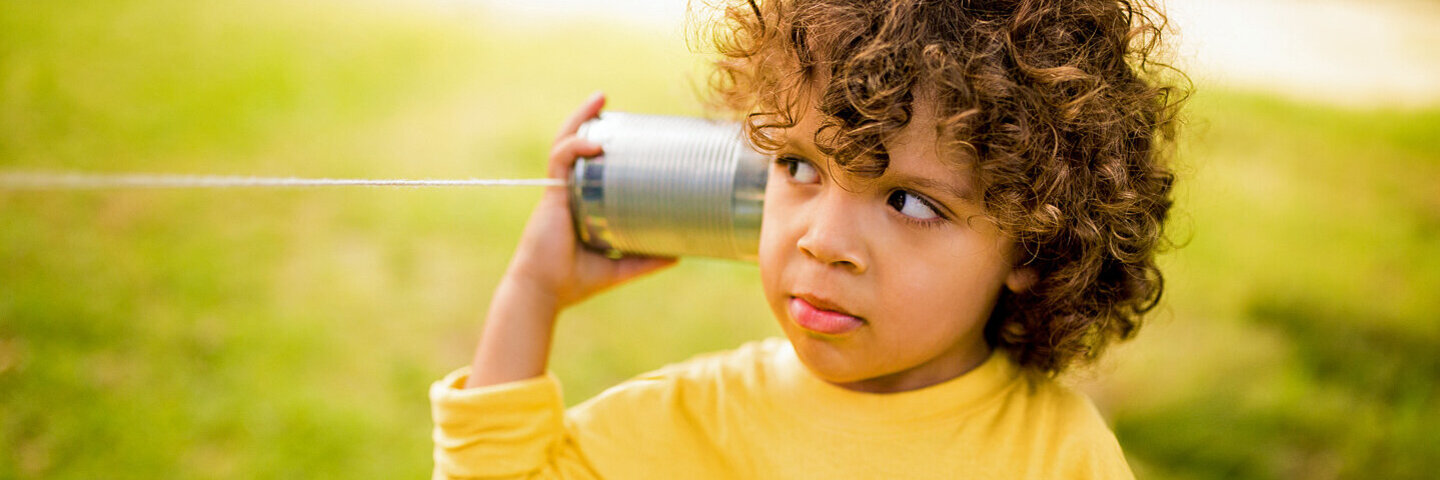 Ein kleiner Junge hält sich eine leere Blechdose wie einen Telefonhörer ans Ohr.