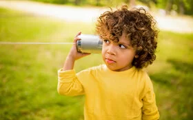 Ein kleiner Junge hält sich eine leere Blechdose wie einen Telefonhörer ans Ohr.