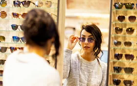 Eine Frau probiert im Brillengeschäft eine Sonnenbrille und schaut in einen Spiegel.