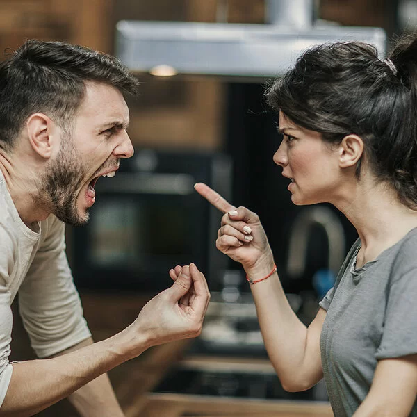 Ein Paar steht sich gegenüber. Beide streiten miteinander und sind sehr wütend. Die Frau richtet den Zeigefinger auf ihren Partner. Der Mann hat den Mund weit geöffnet und schreit. Mit den Fingern der rechten Hand macht er eine Drohgebärde.