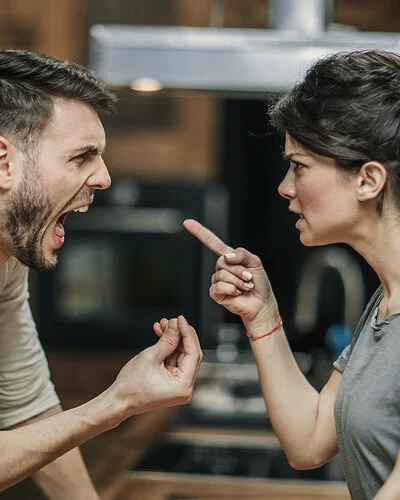 Ein Paar steht sich gegenüber. Beide streiten miteinander und sind sehr wütend. Die Frau richtet den Zeigefinger auf ihren Partner. Der Mann hat den Mund weit geöffnet und schreit. Mit den Fingern der rechten Hand macht er eine Drohgebärde.