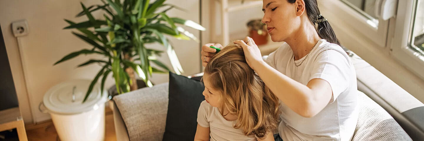 Eine Mutter kämmt die Haare ihrer Tochter mit einem Läusekamm aus.