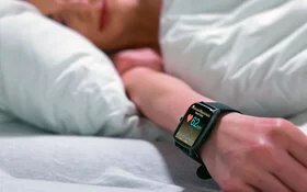Eine schlafende Frau im Bett mit einer Smartwatch am Handgelenk, die die Herzfrequenz misst.