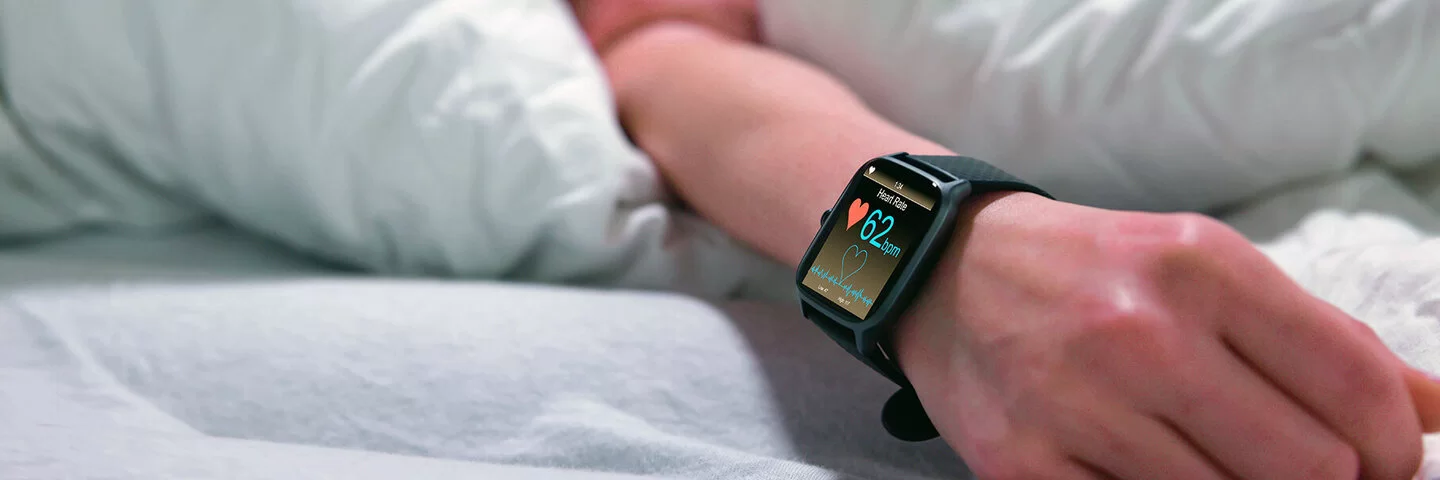 Eine schlafende Frau im Bett mit einer Smartwatch am Handgelenk, die die Herzfrequenz misst.