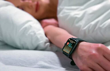 Eine schlafende Frau im Bett mit einer Smartwatch am Handgelenk, die die Herzfrequenz misst.