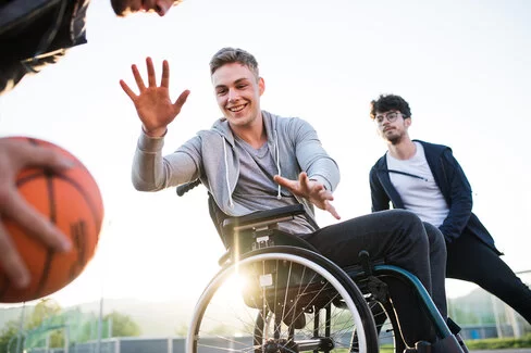 Ein Jugendlicher im Rollstuhl hebt die Arme mit geöffneten Händen und fokussiert den Basketball. Die AOK Hessen fördert den Sport für Menschen mit Behinderung.