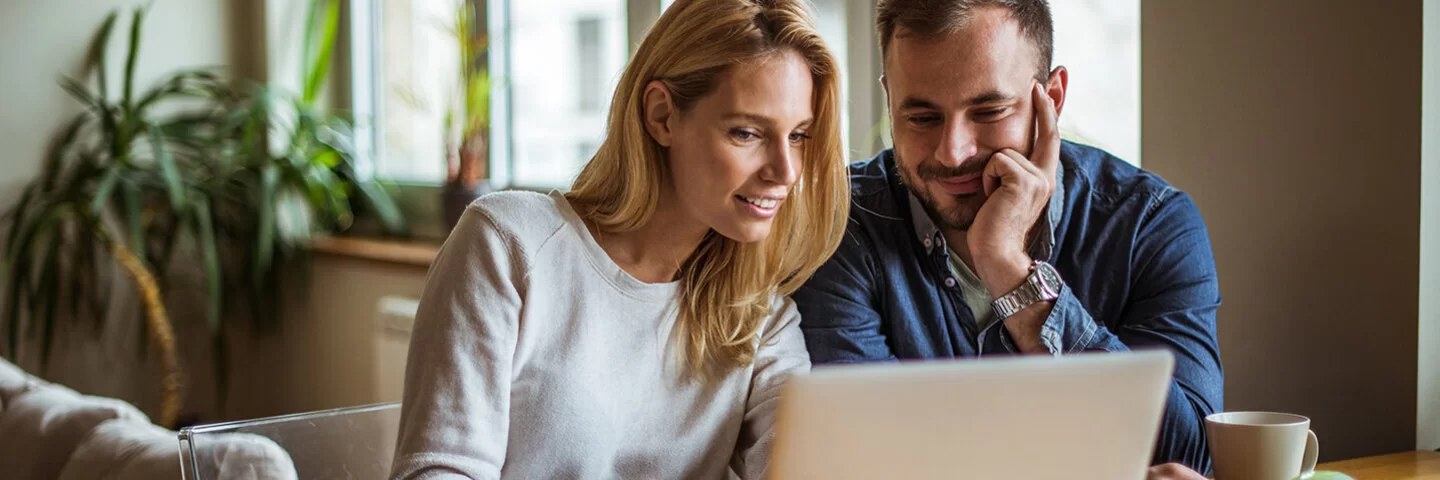 Das Bild zeigt eine Frau und einen Mann, die gemeinsam vor einem Laptop sitzen.