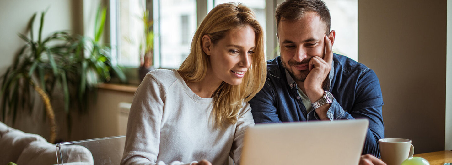 Das Bild zeigt eine Frau und einen Mann, die gemeinsam vor einem Laptop sitzen.