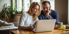 Das Bild zeigt eine Frau und einen Mann, die gemeinsam vor einem Laptop sitzen.