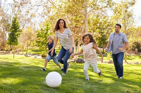 Eine Familie mit zwei Kindern läuft lachend auf einem Rasen einem weißen Ball hinterher