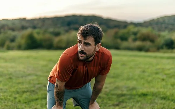 Erschöpfter Sportler in der freien Natur stützt sich auf den Oberschenkeln ab.