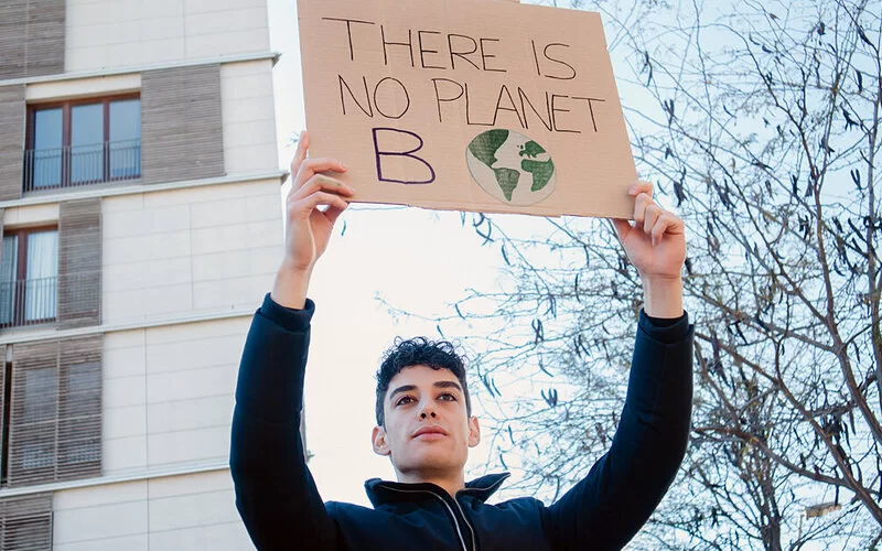 Junger Mann mit Klimaangst hält ein Schild aus Pappe in die Luft.