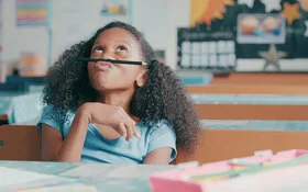 Ein Mädchen mit ADHS sitzt im Klassenzimmer und lenkt sich ab, anstatt sich auf den Unterricht zu konzentrieren.