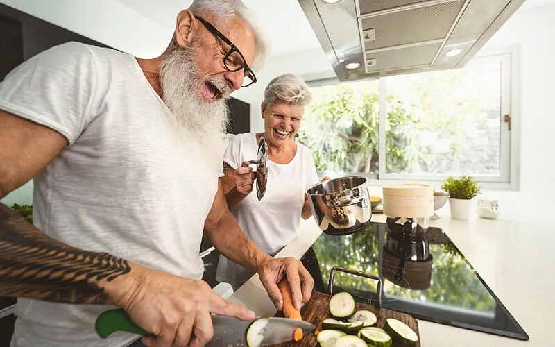 Ein Seniorenpaar kocht zusammen in der Küche und hat Spaß dabei.