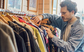 Mann schaut in einem Geschäft durch einen Kleiderständer.