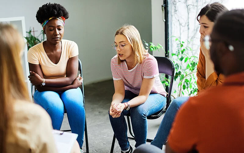 Eine Gruppe junger Menschen sitzt in einem Stuhlkreis bei einer Gruppentherapie.