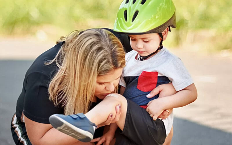 Eine Mama küsst das verletzte Knie des gestürzten Kindes. 