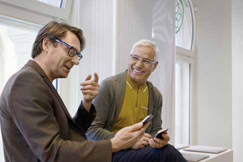 Zwei Männer blicken auf ihre Smartphones. Ihre elektronische Patientenakte können sie mit der App “AOK Mein Leben” aufrufen.