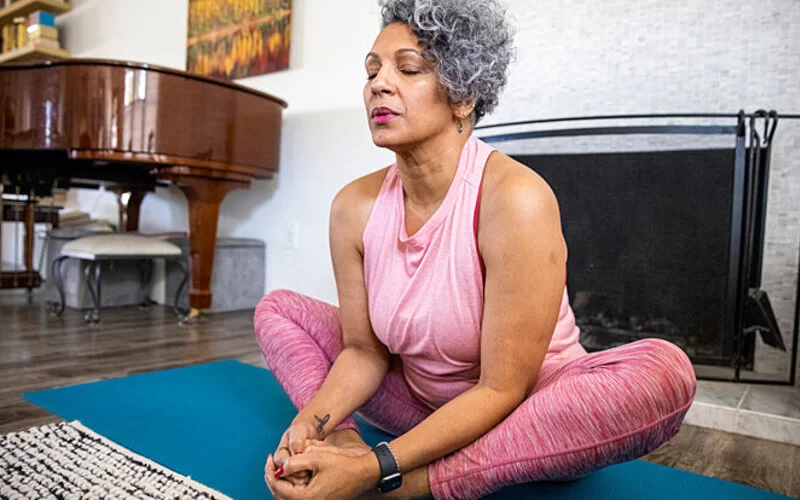 Frau mit Schlafstörungen in den Wechseljahren macht Yoga in ihrem Haus.