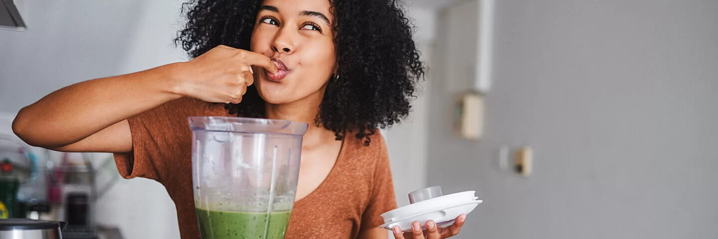 Junge Frau snackt gesund und bereitet sich einen Avocado-Shake zu.