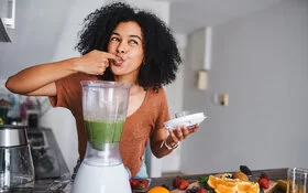 Junge Frau snackt gesund und bereitet sich einen Avocado-Shake zu.