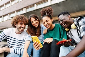 Mehrere Studenten auf dem Campus sitzen entspannt beieinander und lachen miteinander.