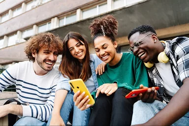 Mehrere Studenten auf dem Campus sitzen entspannt beieinander und lachen miteinander.