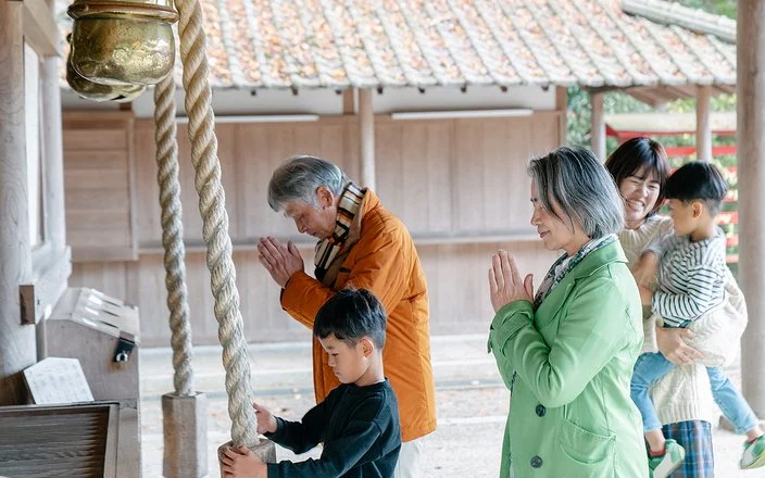 Eine japansiche Familie steht vor einem Tempel, die Erwachsenen beten.