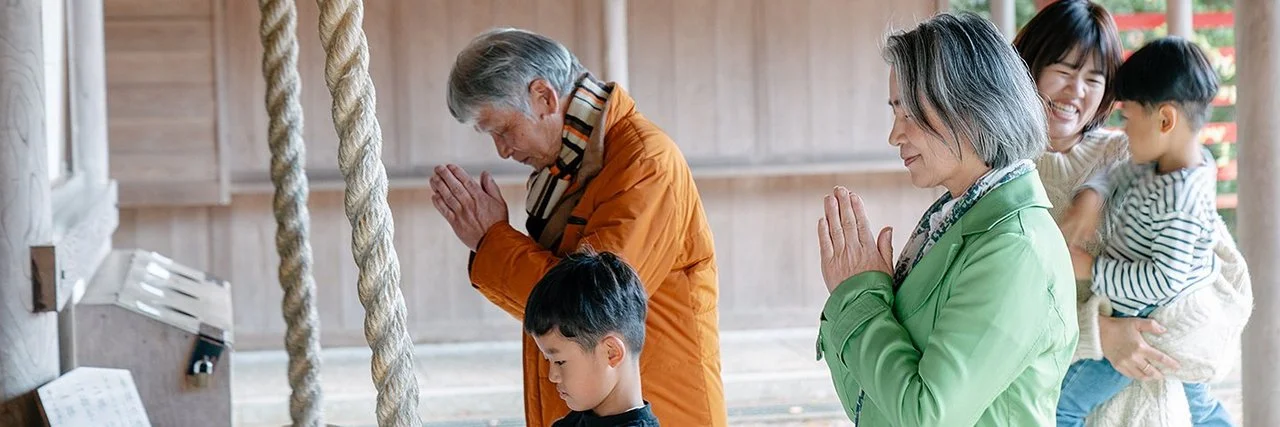 Eine japansiche Familie steht vor einem Tempel, die Erwachsenen beten.