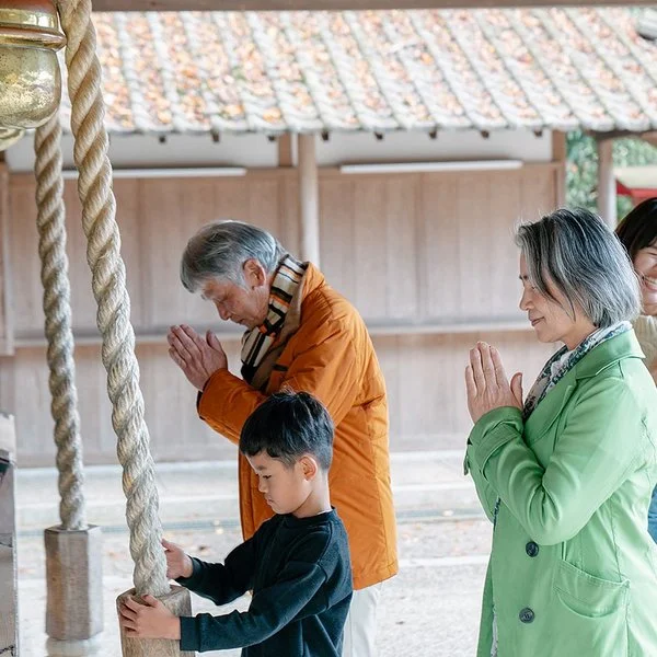 Eine japansiche Familie steht vor einem Tempel, die Erwachsenen beten.
