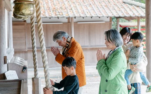 Eine japansiche Familie steht vor einem Tempel, die Erwachsenen beten.