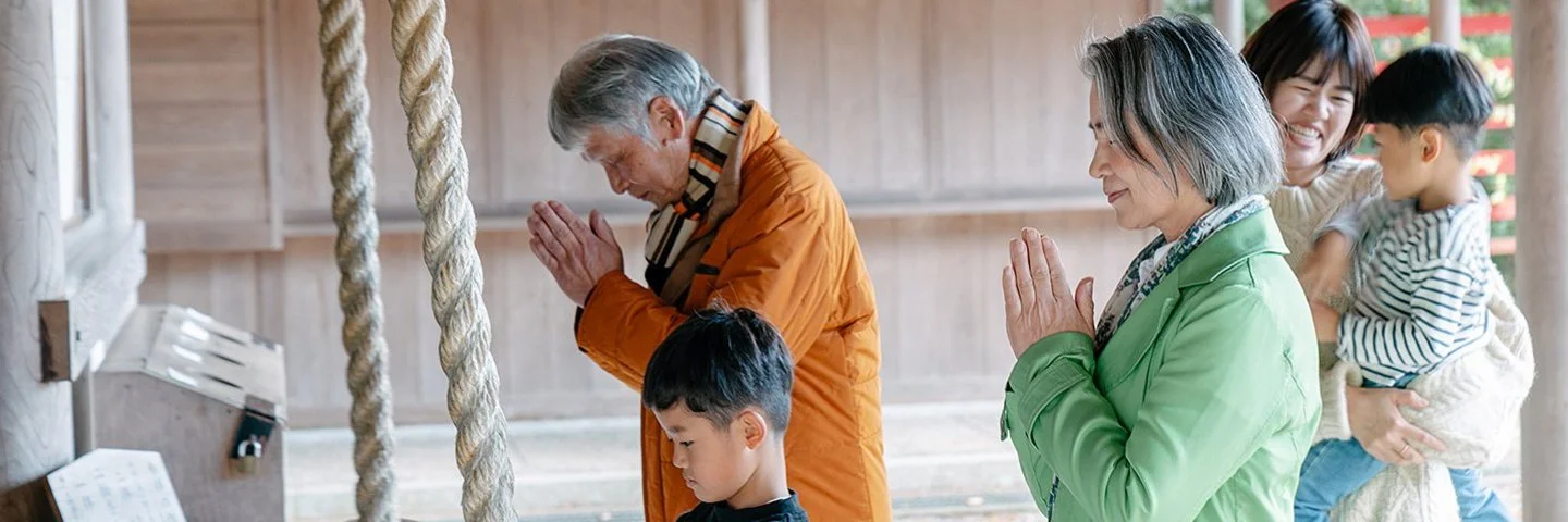 Eine japansiche Familie steht vor einem Tempel, die Erwachsenen beten.