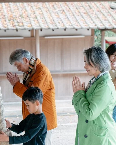 Eine japansiche Familie steht vor einem Tempel, die Erwachsenen beten.