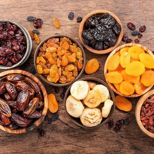 Verschiedene Trockenfrüchte in Schalen auf einem Holztisch aus der Vogelperspektive: Datteln, Feigen, Aprikosen, Pflaumen und verschiedene Rosinen.