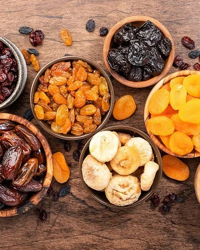 Verschiedene Trockenfrüchte in Schalen auf einem Holztisch aus der Vogelperspektive: Datteln, Feigen, Aprikosen, Pflaumen und verschiedene Rosinen.