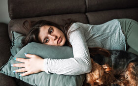 Eine Schwangere mit Angst vor der Geburt liegt traurig neben ihrem Hund auf dem Sofa.