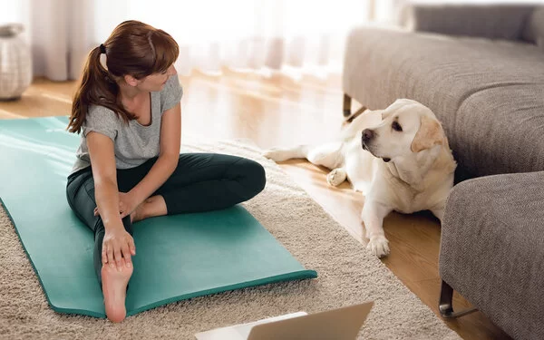 Eine sportliche Frau trainiert zuhause während ihr Hund zusieht.