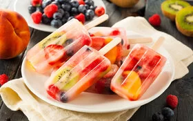 Fruchtiges selbst gemachtes Wassereis am Stiel mit Kiwi und Beeren verfeinert liegt auf einem Teller.