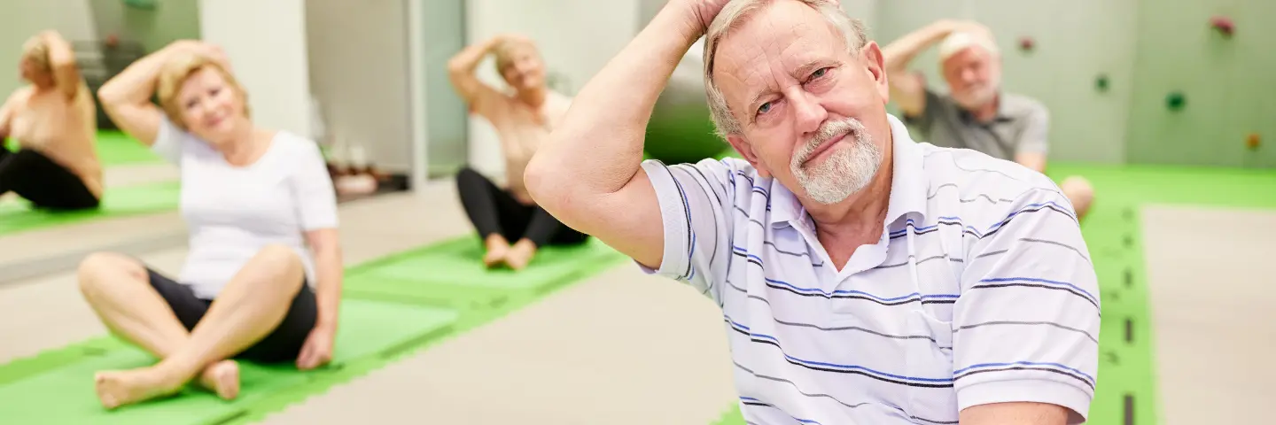 Vier Männer und Frauen sitzen auf Gymnastikmatten und machen eine Dehnübung.