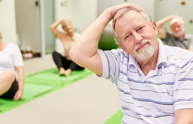 Vier Männer und Frauen sitzen auf Gymnastikmatten und machen eine Dehnübung.