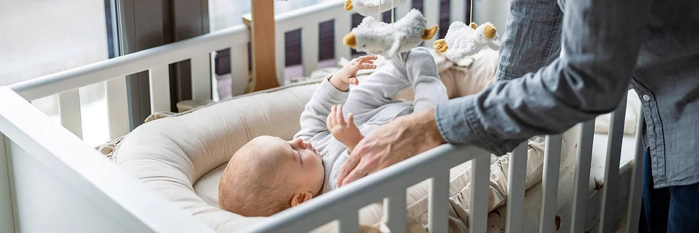 Ein Vater kümmert sich um sein Baby, das in einem Babybett liegt.