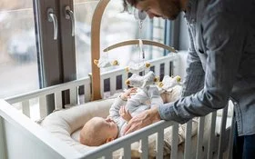 Ein Vater kümmert sich um sein Baby, das in einem Babybett liegt.