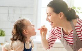 Gesunde Ernährung: Eine Mutter hält ein Stück Tomate in der Hand und gibt sie ihrem Kind.