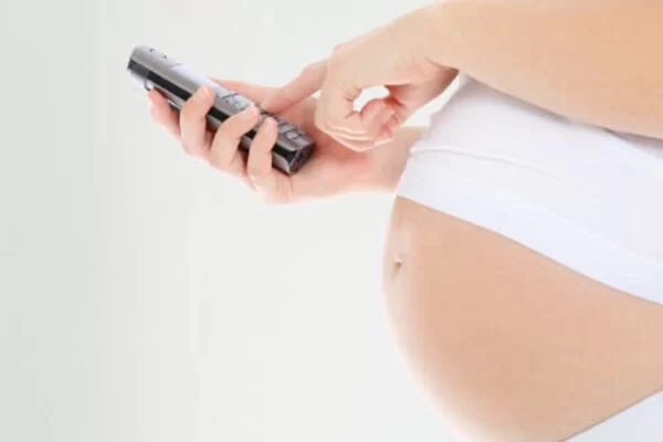 Man sieht eine schwangere Frau, die vor ihrem Babybauch ein Telefon hält ein und mit ihrer linken Hand eine Nummer wählt.