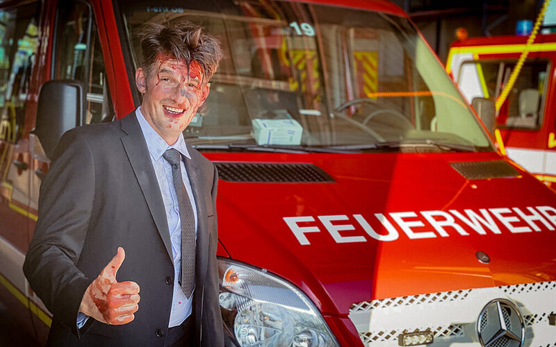 Schauspieler Dr. Christoph-Gérard Stein mit Blut im Gesicht vor einem Feuerwehrauto.